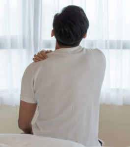A man sits on his bed holding his shoulder that may have a rotator cuff injury